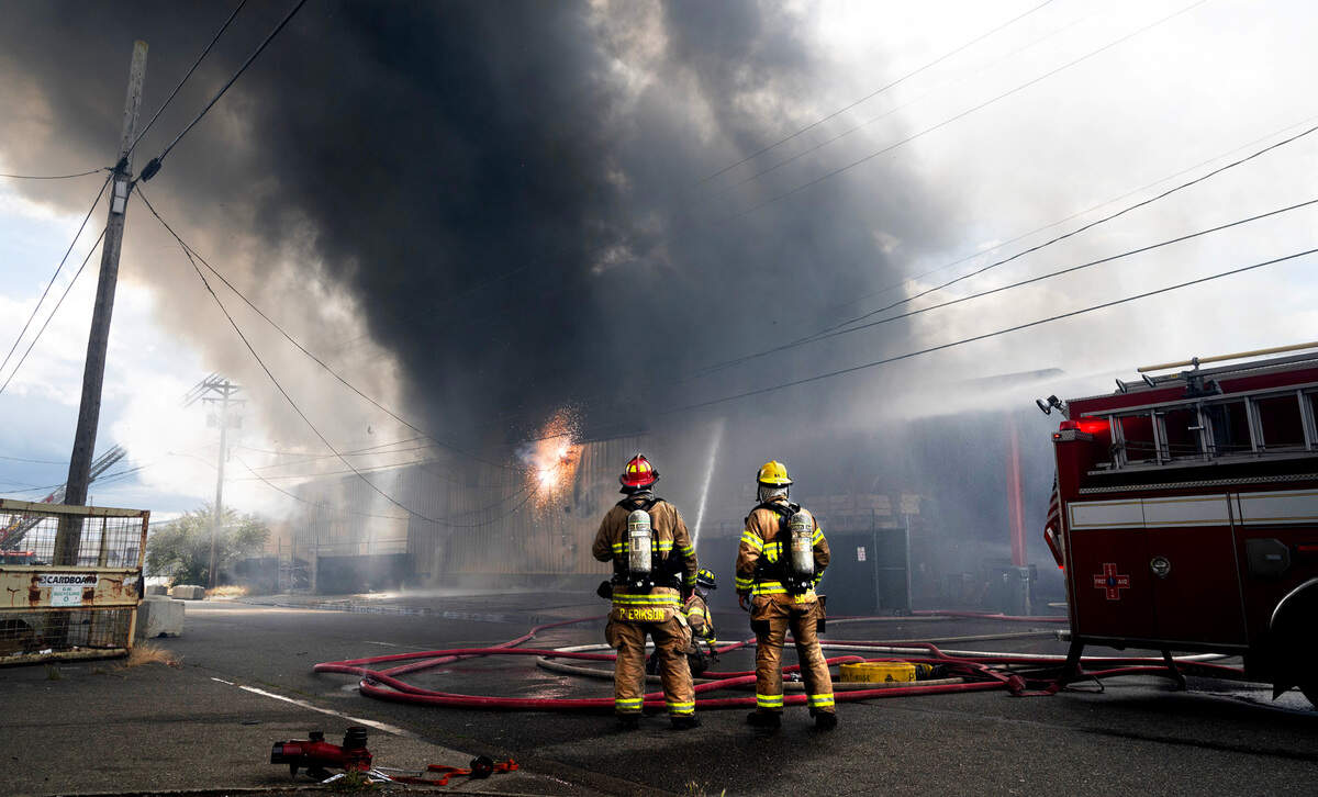Firefighters watch as electric lines explode during a large warehouse fire at an auto shop on Adams Street in Southwest Tacoma, Washington, on Wednesday, Aug. 30, 2023.