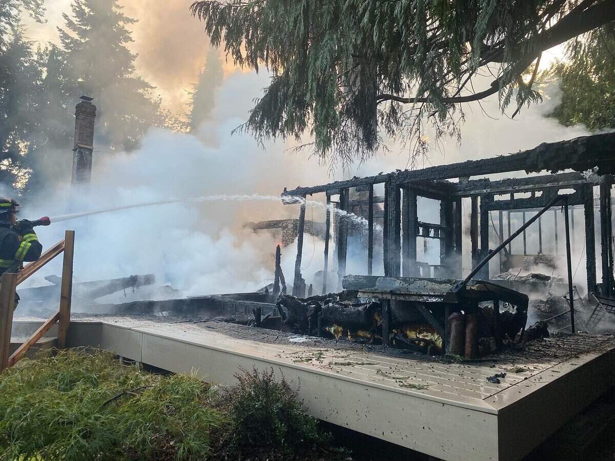 A firefighter extinguishes a house fire July 29, 2023 on the 21100 block of Snag Island Drive E.