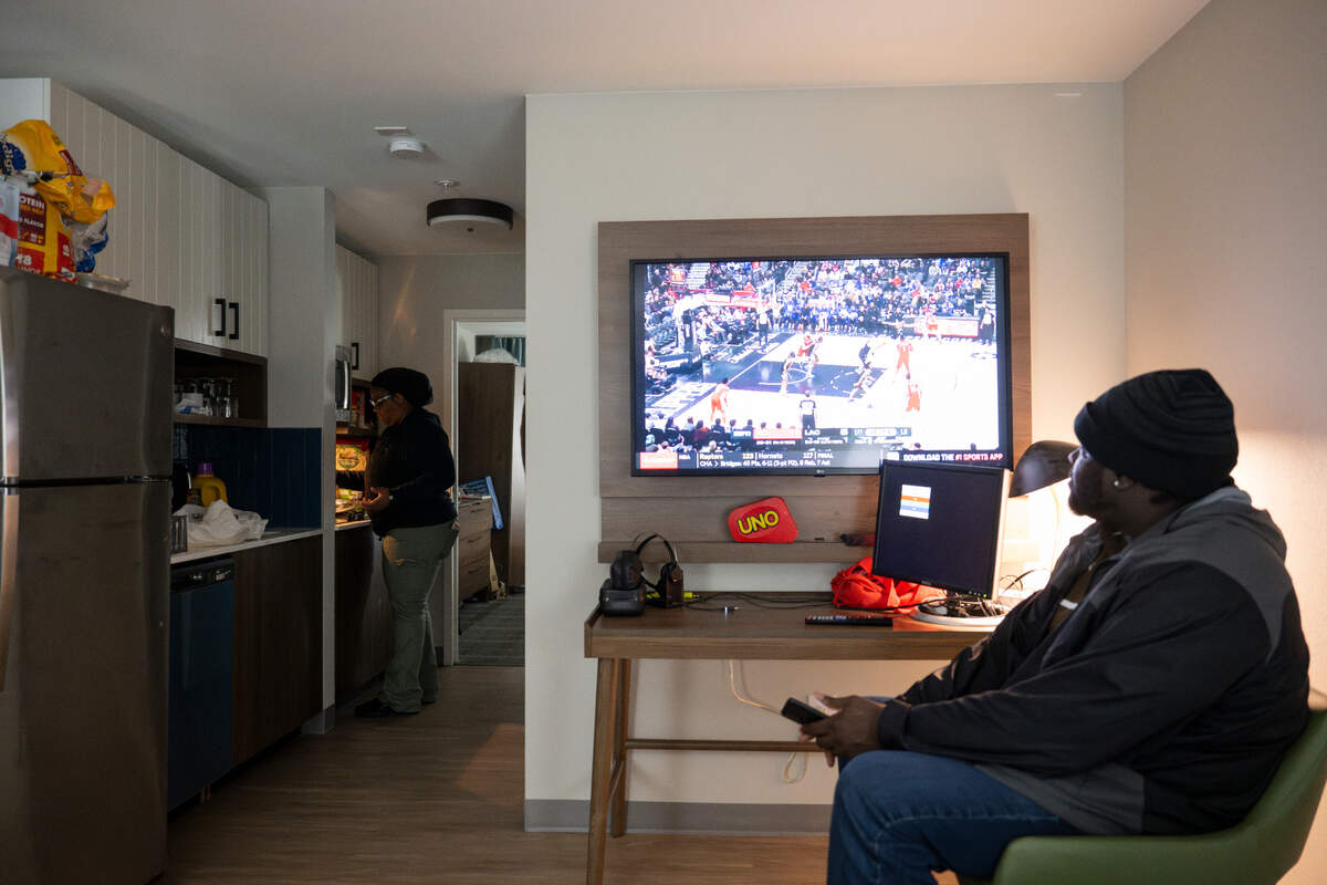 Renee Niles starts preparing dinner as husband Alphonso watches basketball at Staybridge Suites, on Wednesday, Feb. 7, 2024, in Federal Way, Washington. They, their three sons and dog have been living in the hotel for five months after being displaced from their home in Spanaway due to water damage.