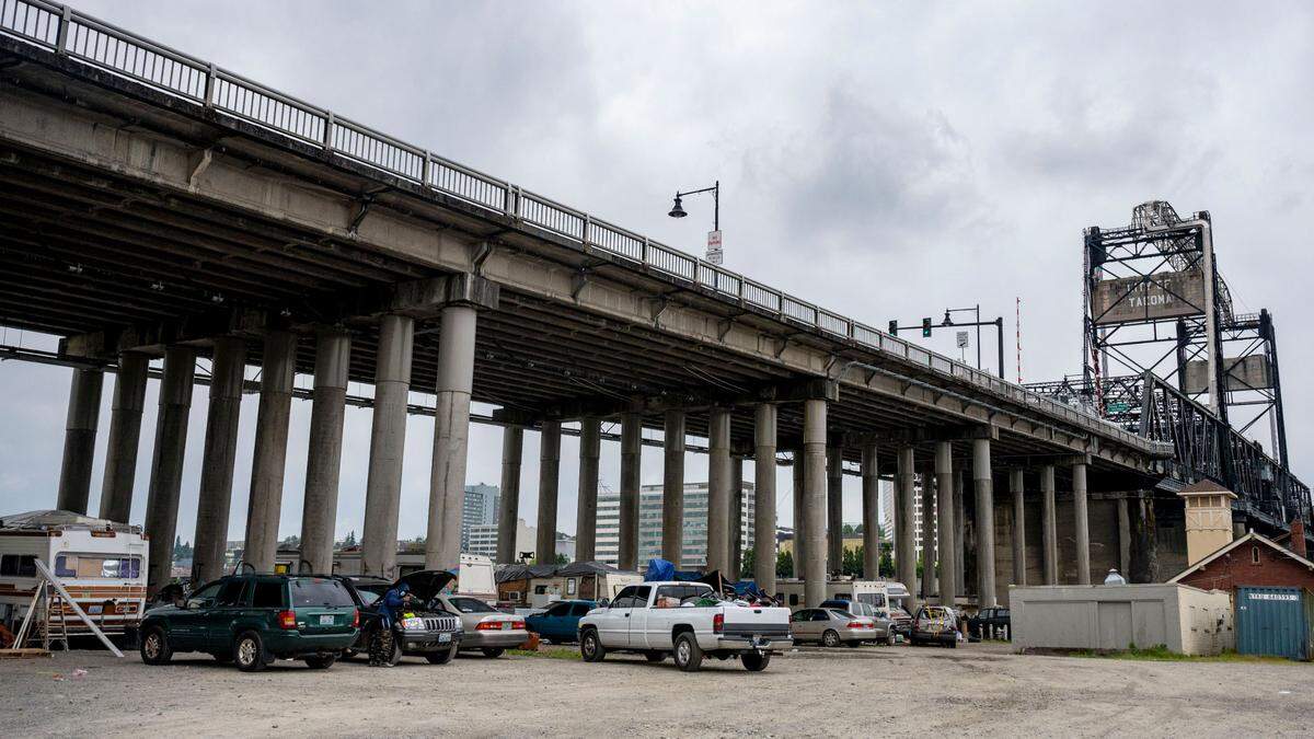 A man works on his vehicle as cars, trucks and trailers are scattered in a homeless encampment underneath the north side of the Murray Morgan Bridge on Wednesday, June 15, 2022, in Tacoma, Wash.
