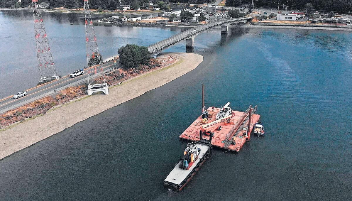 A tugboat pushes a barge across the Purdy Bridge into Burley Lagoon. Tacoma Power is replacing the 92-yer-old power line towers, left, along Henderson Bay and Burley Lagoon in Purdy, Wash., by the end of July 2018. They will be replaced by 170-foot steel mono poles like the tower on Case Inlet near Allyn, Wash.