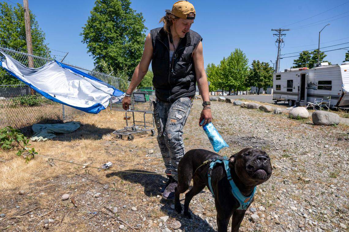 Jesse Moehringer holds onto his dog after trying to coax it into the shade under a tarp outside his RV parked on South Trafton Street on Tuesday, June 6, 2023, in Tacoma, Wash.