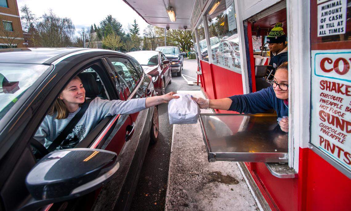 Bella Hinton, right, hands Shawna Cole her order as cars queue up at the Frisko Freeze drive-thru window. The 70-year-old fast food icon is weathering the coronavirus crisis the same way it alway has – serving up Tacoma’s favorite greasy burgers and fries.