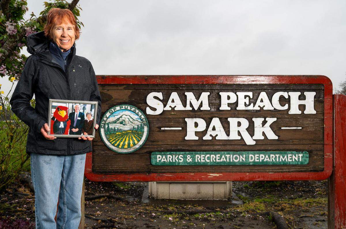 Kathi Peach-Cassidy, daughter of Sam Peach, a former Puyallup mayor who passed away in February at the age of 94, poses for a portrait with a photograph of her father at Sam Peach Park in Puyallup, Wash. on Thursday, May 5, 2022.