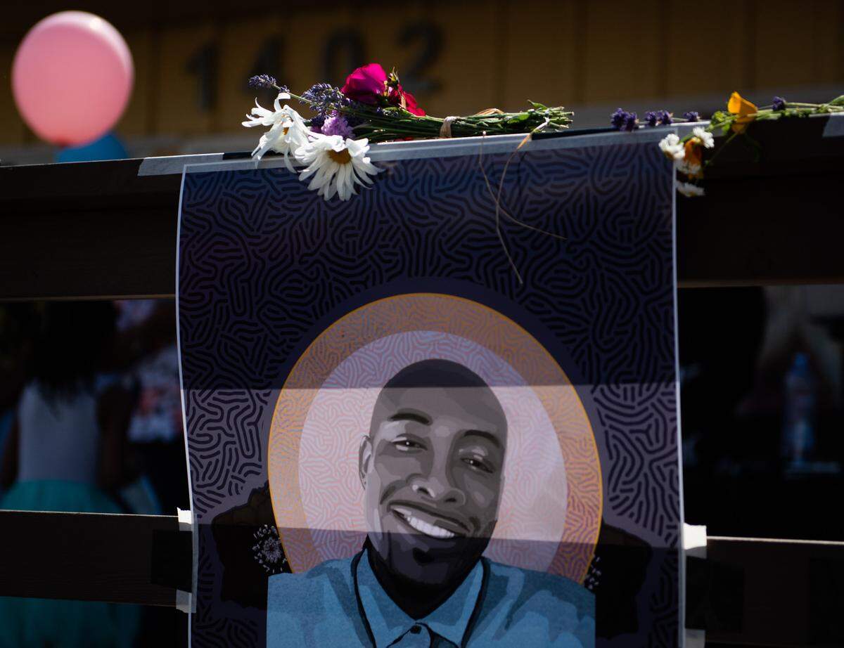 Flowers are left by a poster of Manuel Ellis during a Father’s Day celebration in honor of Manuel Ellis at Go Philly Cheesesteaks and Wings in Tacoma, Wash., on Sunday, June 21, 2020