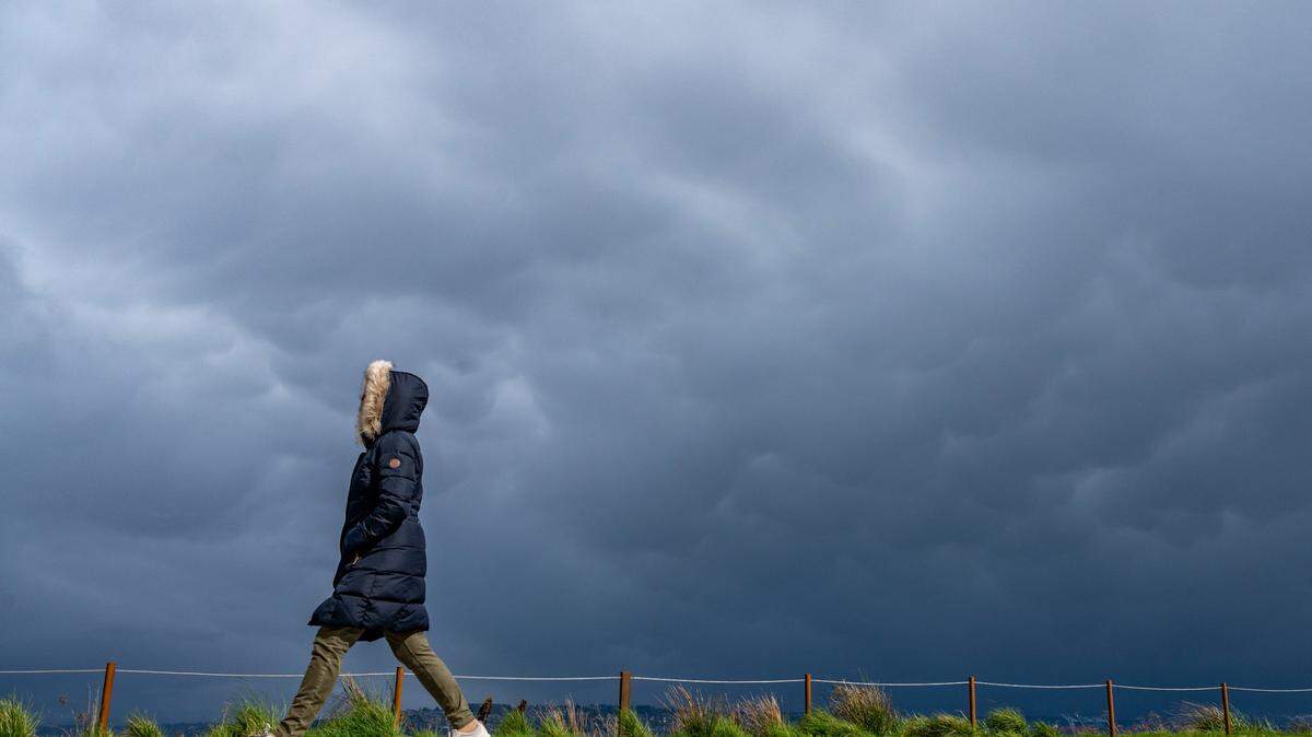 A woman walks along the pathway at Dune Peninsula as gusts of wind blow in from the south and rain falls to the north on Monday, April 4, 2022, in Tacoma, Wash.
