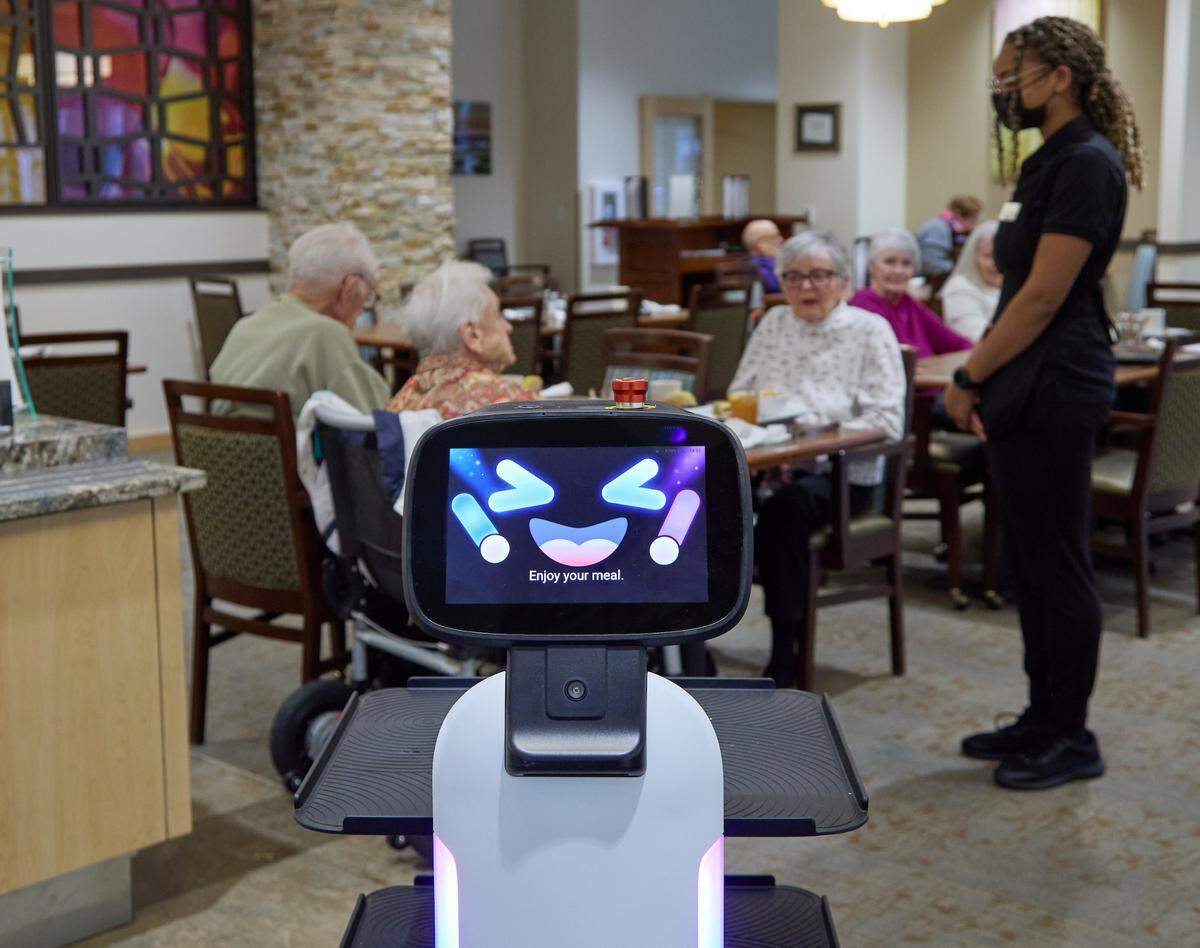 GenCare Lifestyle server Destiny Williams (right) chats with Point Ruston residents Ruth Di Domenico, Deck Thorn and Sally Kelly while they eat. Williams aided by a Segway robot that transports food from the kitchen to the table, Thursday, Dec. 8, 2022, in Tacoma.