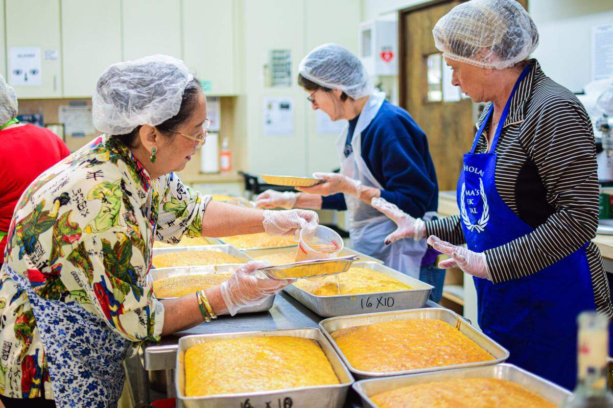 Merrliee Pangis (left) and Karen Samaras soak freshly baked lemon cakes with ouzo syrup at St. Nicholas in 2024. They have been among hundreds of volunteers who start baking pastries in the spring each year for the fall festival, now in its 62nd year.