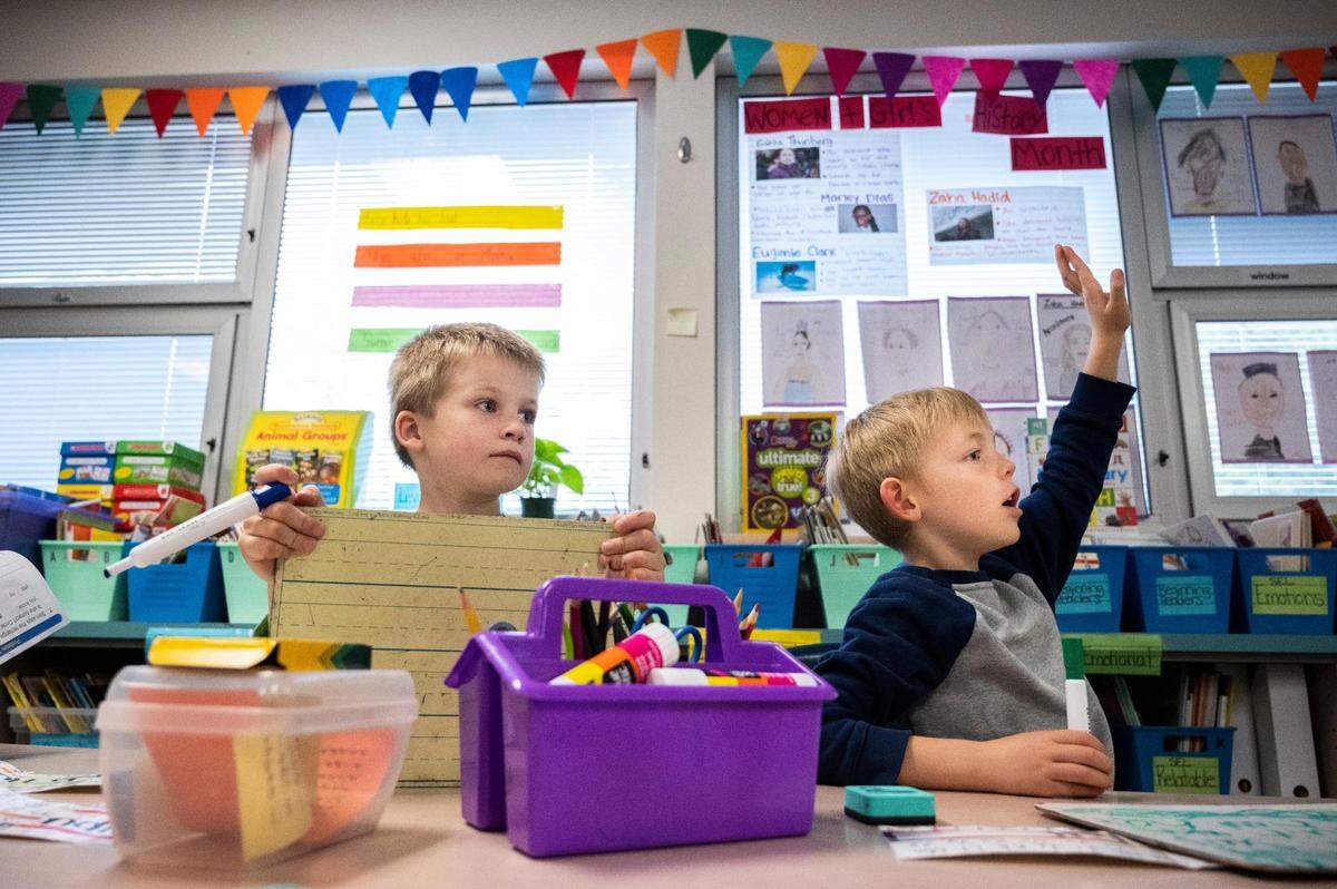 First grader Caleb Hubbard, left, watches his teacher, Tracy Morrison, write on the board, while his classmateTeddy Felt, right, raises his hand to answer a question during their Enhanced Core Reading Instruction training (ECRI) class at Harbor Heights Elementary in Wollochet, Wash. on Friday, June 3, 2022.