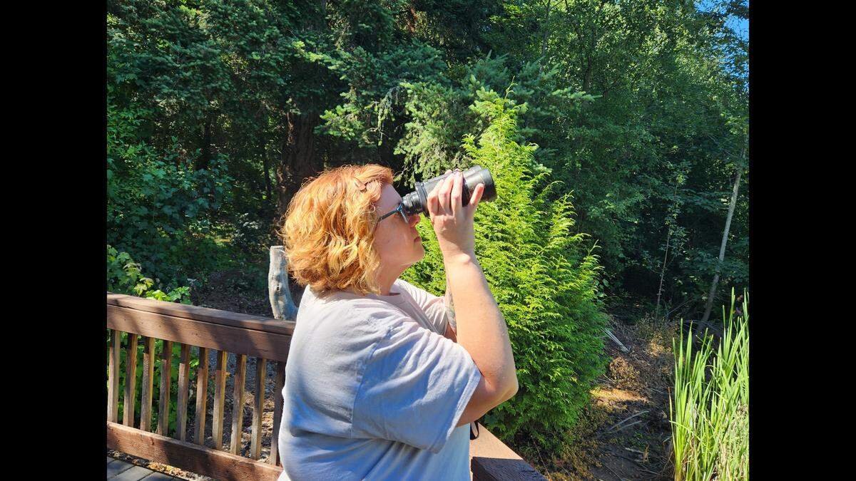 Suzanne Harkness uses binoculars to observe nature on July 13, 2023, at Adriana Hess Wetland Park in University Place.