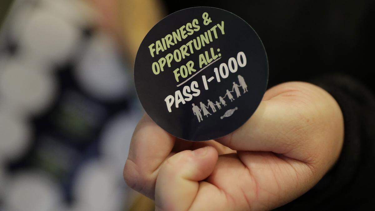 A volunteer holds a sticker showing support for Initiative 1000 outside a joint Washington state House and Senate committee on April 18. Ten days later, both chambers adopted I-1000 and Gov. Jay Inslee signed it.