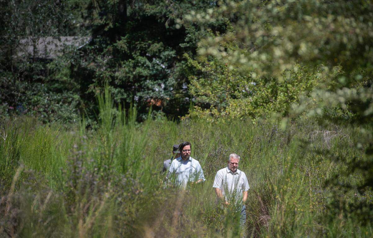Duke Paulson (right) of the Tacoma Rescue Mission walks through the site of a proposed 285-unit tiny home village in Spanaway, Washington, on Tuesday, Aug. 1, 2023. The project on property surrounded by wetlands near Spanaway Lake has drawn scrutiny for its location, costs, long-term funding, and the process that allowed it to be approved.