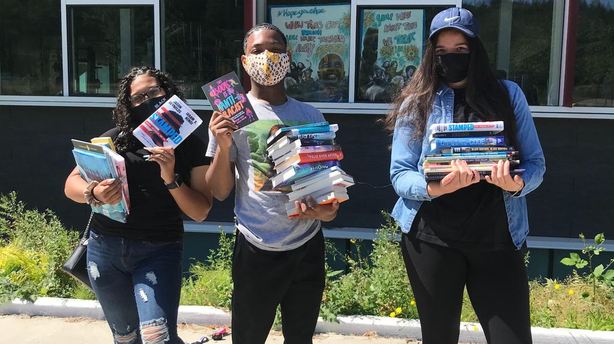 Three student volunteers show the diverse books they are helping distribute to students across Tacoma.