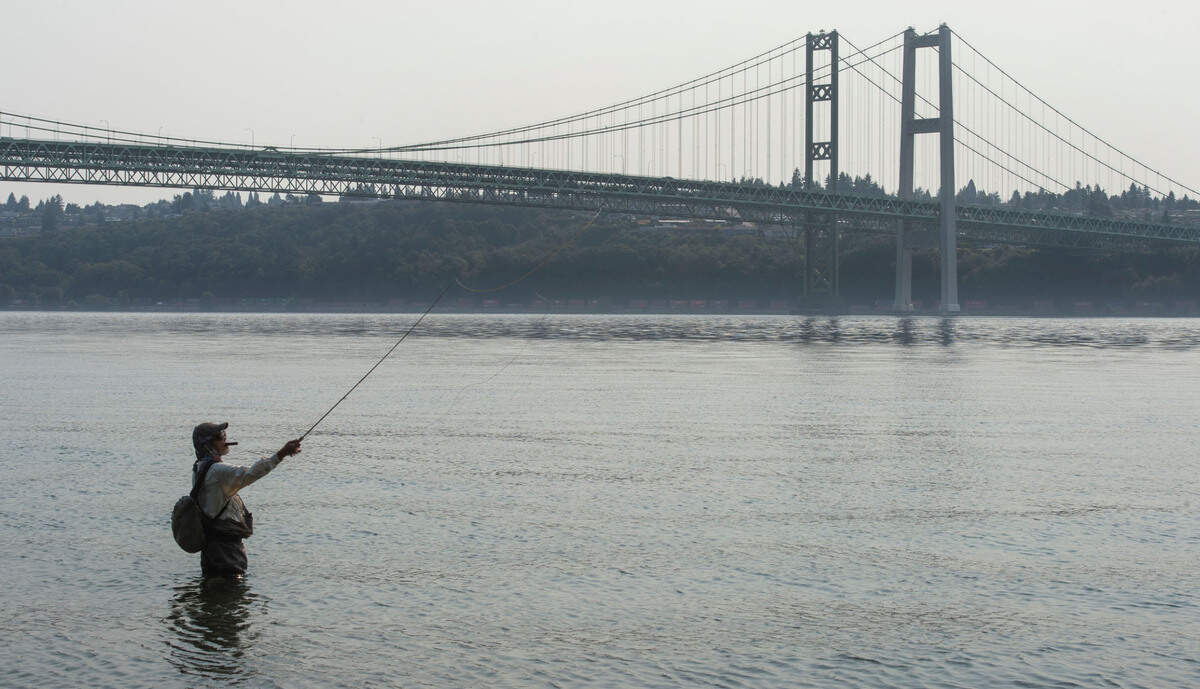 Light haze from wildfire smoke partially obscures this fisherman’s view of the Tacoma Narrows Bridge as seen from Narrows Park in Gig Harbor on Friday, August 13, 2021. Wildfire smoke is beginning to accumulate in parts of Western Washington, but Pierce and Thurston counties should escape the worst of it.