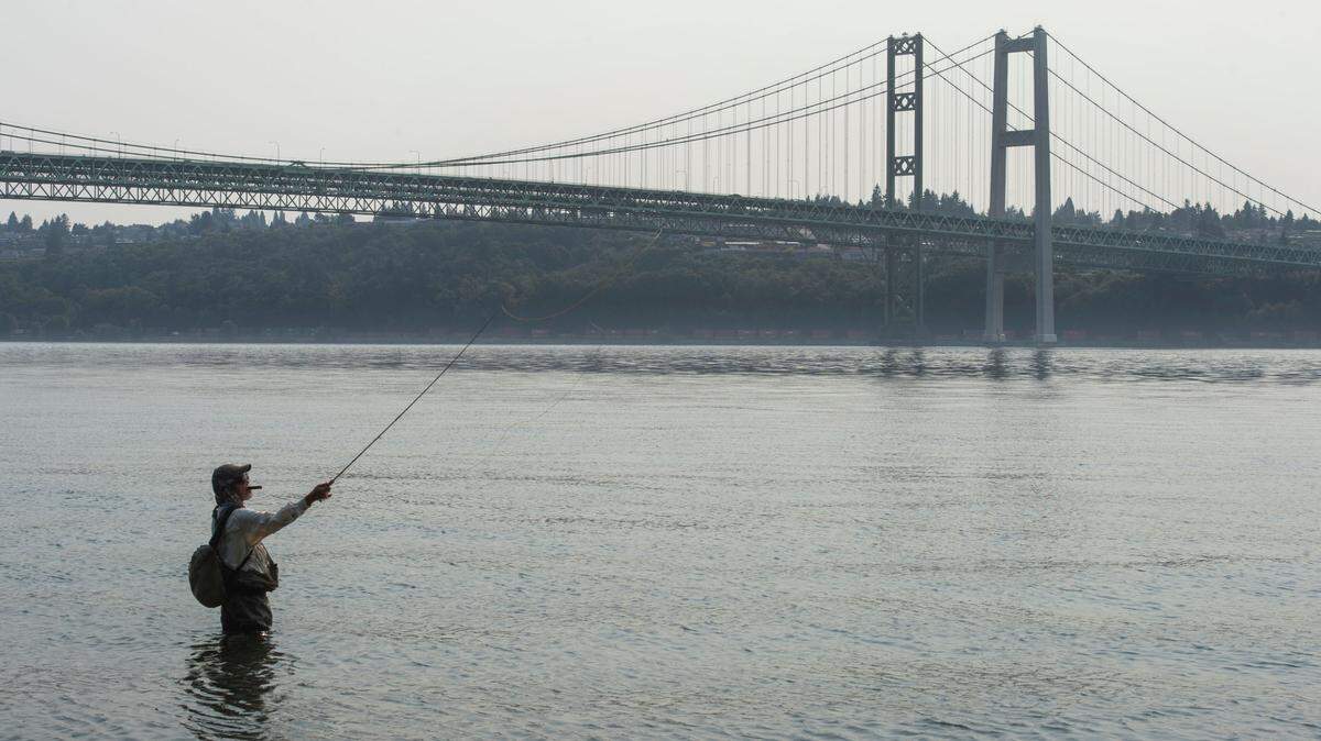 Light haze from wildfire smoke partially obscures this fisherman’s view of the Tacoma Narrows Bridge as seen from Narrows Park in Gig Harbor on Friday, August 13, 2021.