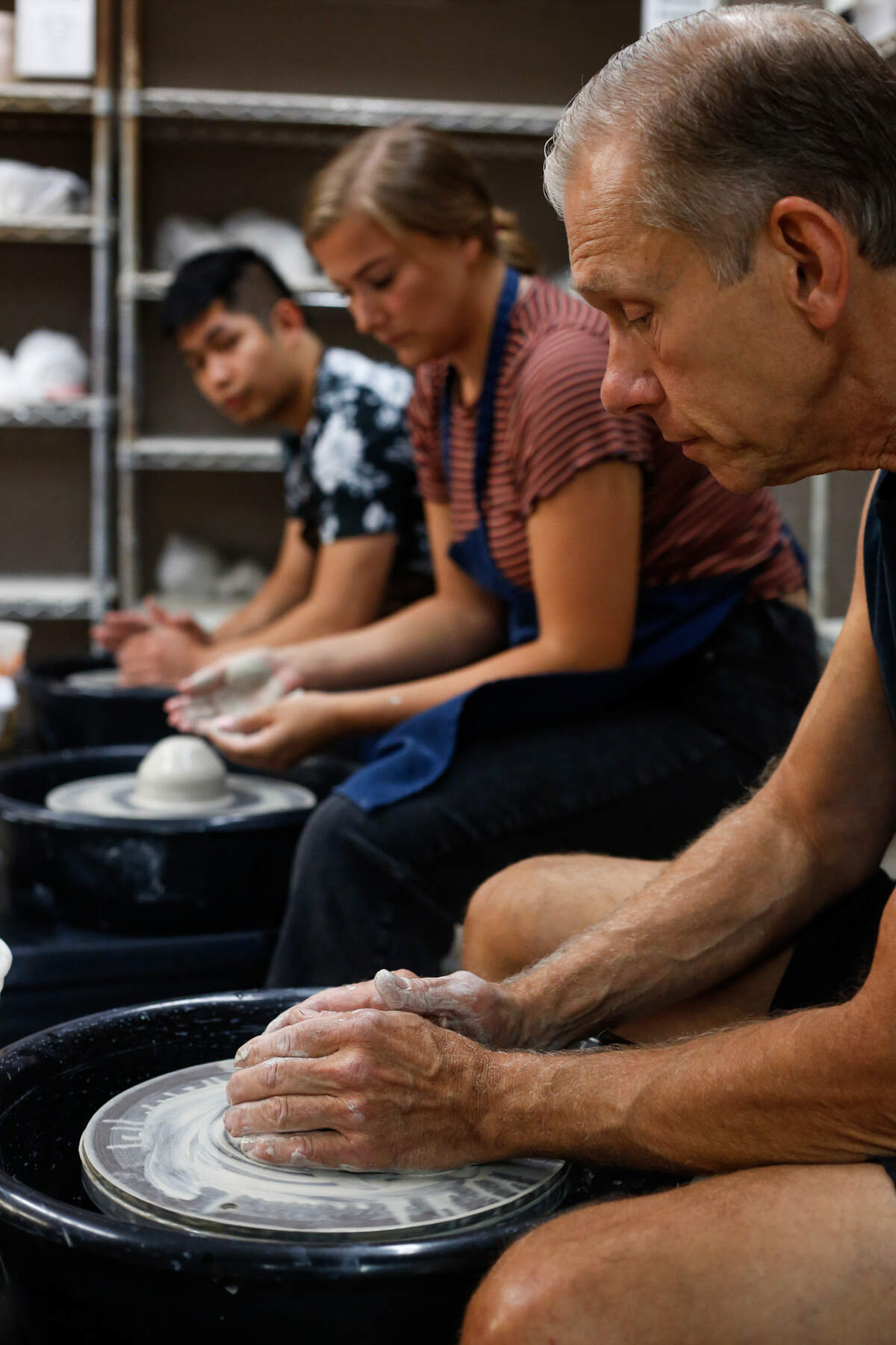Murk Hudak (right), potter and co-owner of the Throwing Mud Art Gallery, teaches new students in his pottery class the correct way to form their hands over clay Aug. 10, 2019.