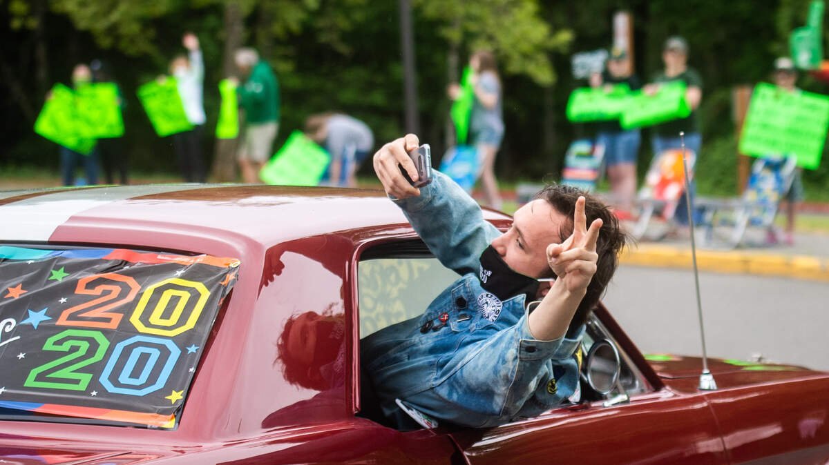 Brandon Grover takes a selfie as he leans out of a car window after picking up his cap and gown at Peninsula High School. Graduating seniors at Peninsula High School received their caps, gowns, and signs in a car parade as they were cheered on by PHS staff and members of the community.