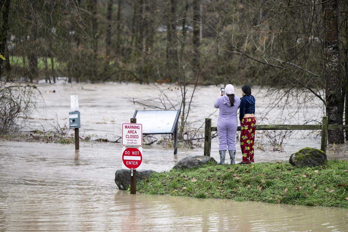 Mother and daughter Katrina and Nayeli Valdovinos, who live nearby, watch as the water continues to rise along Puyallup Riverwalk Trail, on Thursday, Dec. 11, 2025, in Puyallup, Wash.