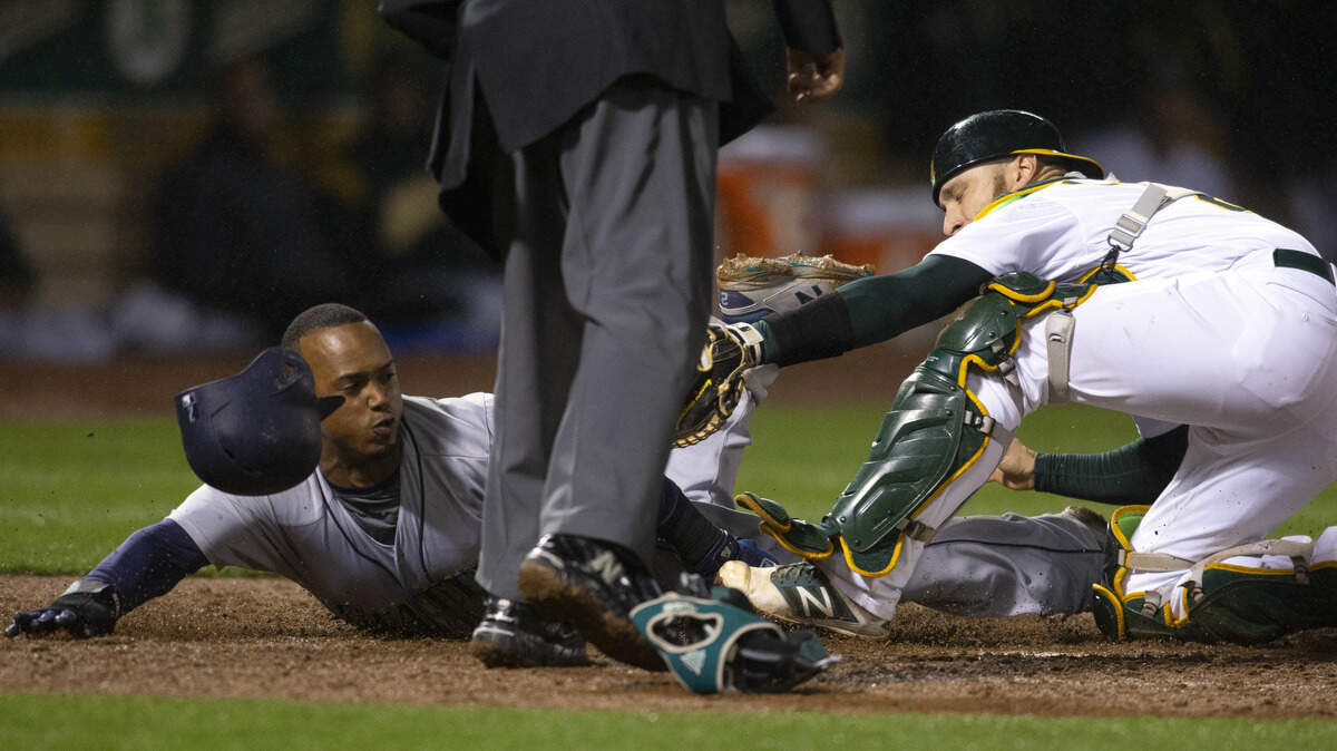 Seattle Mariners' Jean Segura slides safely home ahead of the tag by Oakland Athletics catcher Jonathan Lucroy during the 10th inning of a baseball game Tuesday, May 22, 2018, in Oakland, Calif. Segura scored on a double by Guillermo Heredia. The Mariners won 3-2. (AP Photo/D. Ross Cameron)