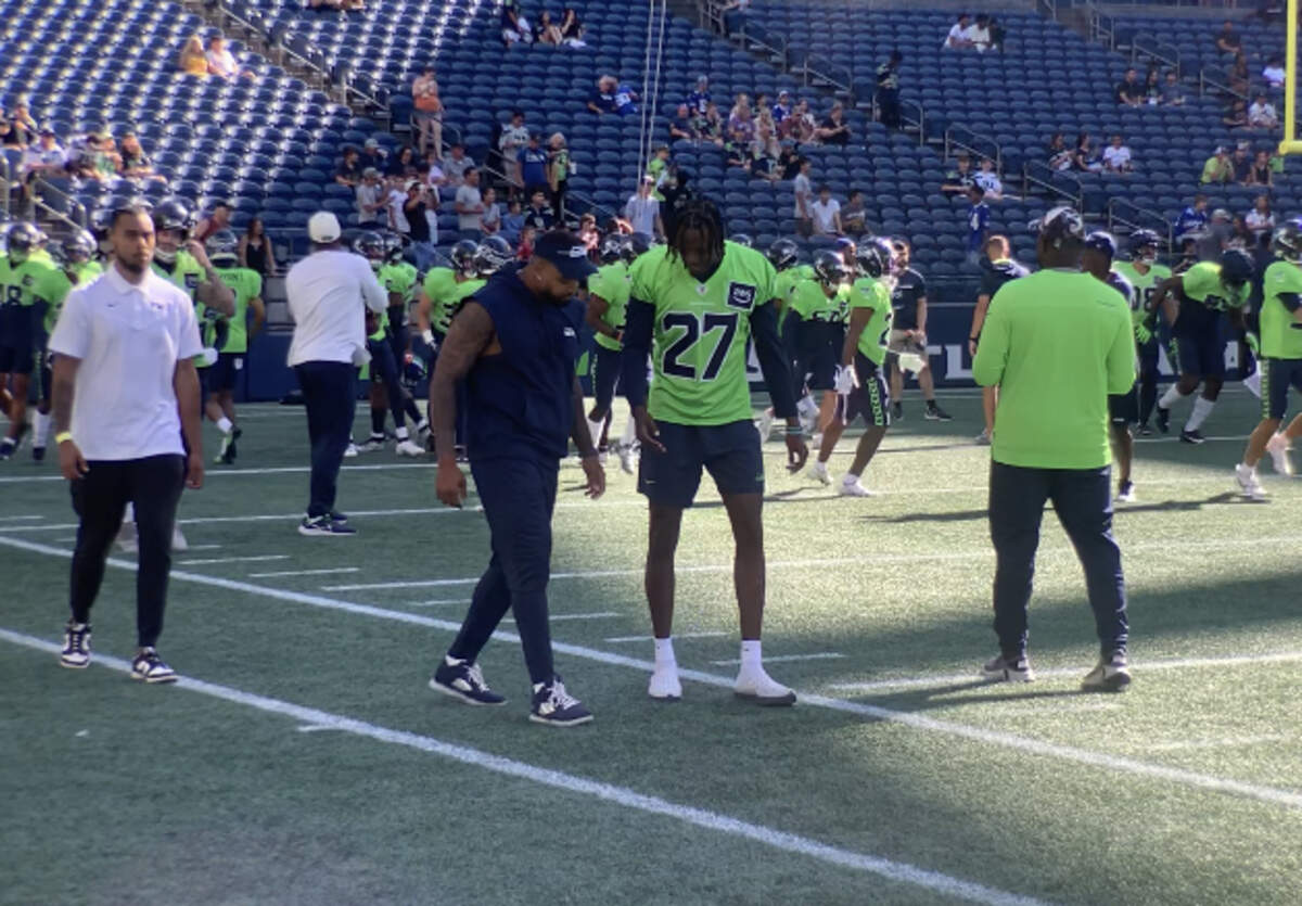 Riq Woolen (27) talks with Jamal Adams before both defensive backs watched the Seahawks’ annual mock-game scrimmage at Lumen Field in Seattle Aug. 4, 2023. Woolen and Adams began training camp on the physically-unable-to-perform list.