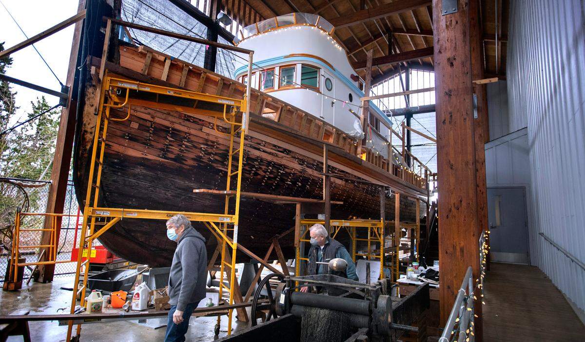 Volunteers Dave Federighi (left) and Ken Hoy work below the the 65-foot Shenandoah fishing vessel under restoration at the Harbor History Museum in Gig Harbor, Washington, on Thursday, Feb. 3, 2022.