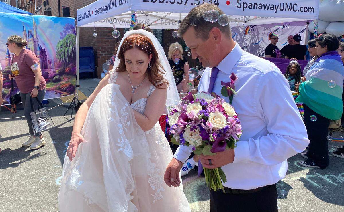 Newlyweds Stephanie and Jesse Peckham of Yelm walk through the Tacoma Pride festival on Saturday, July 8, 2023.
