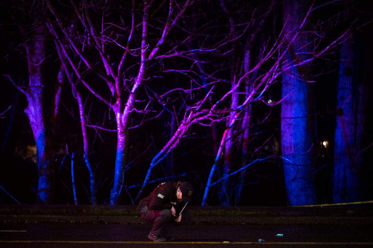 A detective from the Tacoma Police Department looks for evidence along street as law enforcement personnel investigates the scene of a shooting near the intersection of Portland Avenue and East 40th Street on Thursday, Jan. 12, 2023, in Tacoma, Wash.