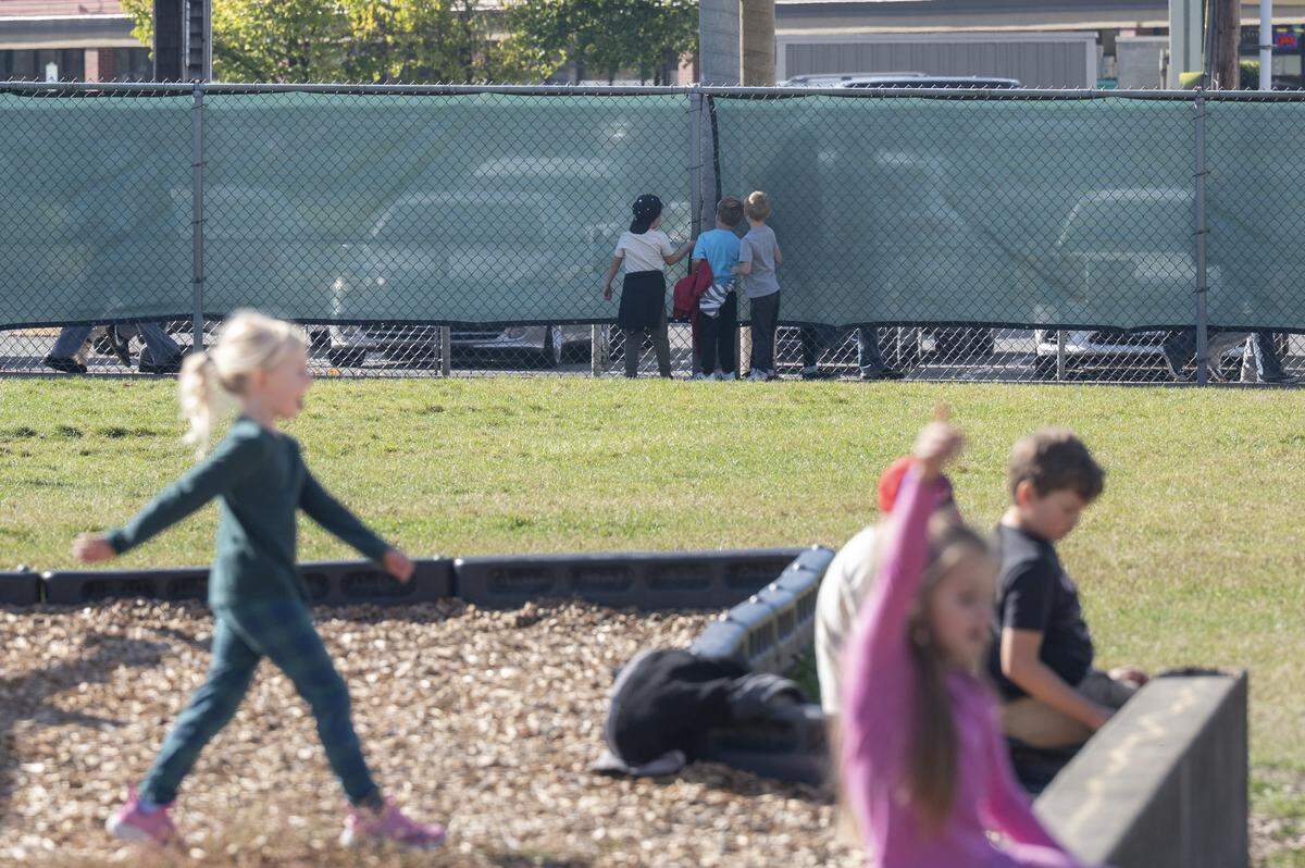 Orting Elementary School students stand by the fence as Orting High School students walk between classes on the other side on Wednesday, Oct. 15, 2025, in Orting, Wash. The elementary school added the green lining to the fence to limit interactions between younger and older students.