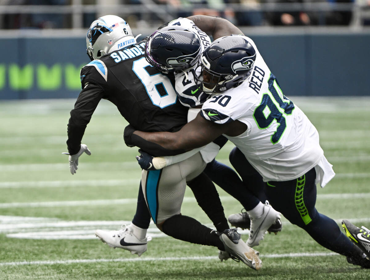 Carolina Panthers running back Miles Sanders (6) is brought down by Seattle Seahawks cornerback Devon Witherspoon (21) and defensive tackle Jarran Reed (90) during the second quarter of the game at Lumen Field, Sunday, Sept. 24, 2023, Seattle, Wash.