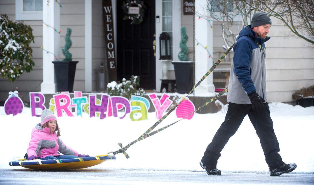 Jesse Lewis gives ride to his daughter, Elise, 7, as they walk through the snow in DuPont, Washington, on Tuesday, Dec. 28, 2021.