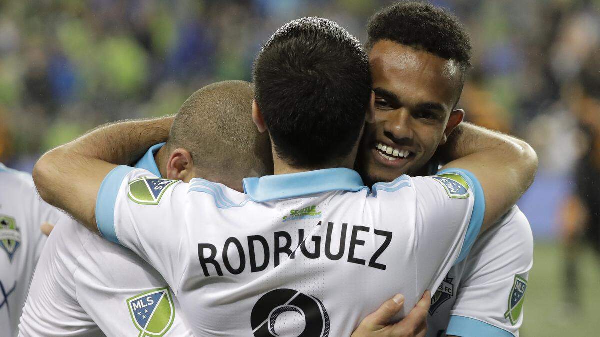 Seattle Sounders midfielder Victor Rodriguez is hugged by captain Osvaldo Alonso, left, and midfielder Handwalla Bwana, right after Bwana assisted Rodriguez for his second goal in the second half of an MLS soccer match against the Houston Dynamo, Monday, Oct. 8, 2018, in Seattle. The Sounders won 4-1. (AP Photo/Ted S. Warren)