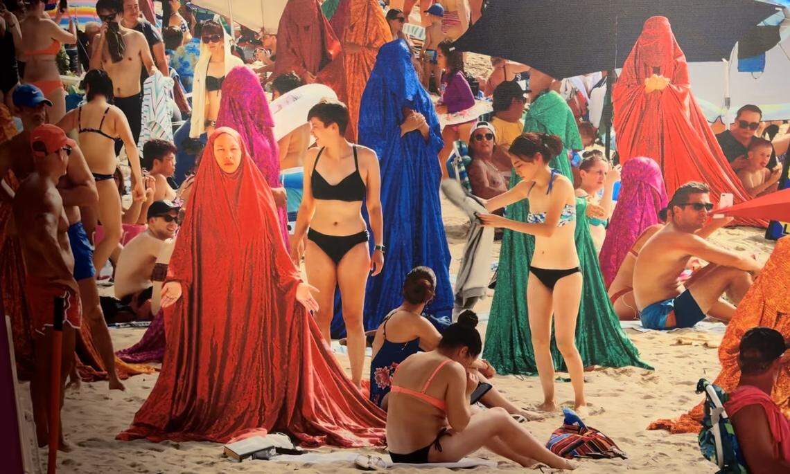 Anida Yoeu Ali wears “The Red Chador” on a crowded beach in Australia.