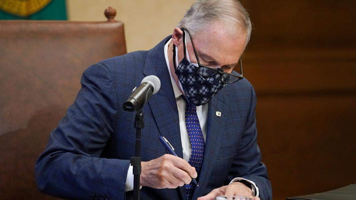 Washington Gov. Jay Inslee signs the first bill to be signed into law during the 2021 legislative session, Monday, Feb. 8, at the Capitol in Olympia, Wash. The measure increased the minimum weekly benefit for unemployed workers during the ongoing coronavirus pandemic and prevents a dramatic increase in unemployment taxes paid by businesses.