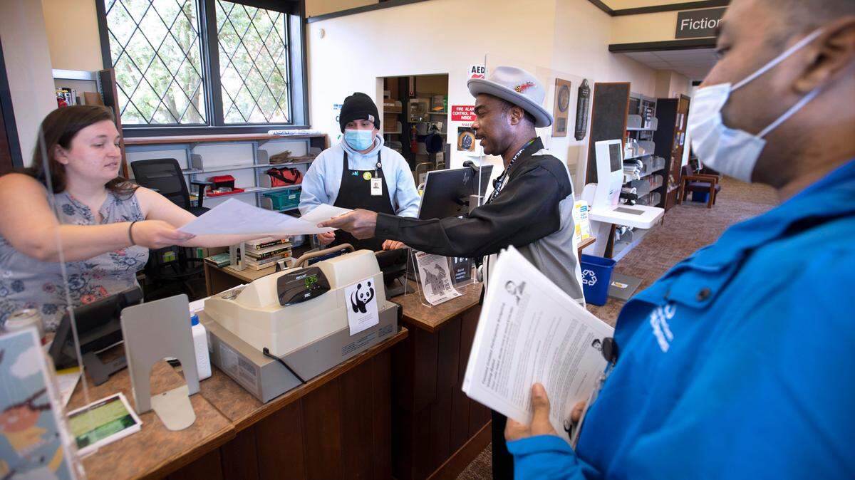 Marcus Taylor and James Johnson (far right) pass out informational posters about the Tacoma Creates election to library assistant Kate Lewis and associate JC Esquinca at the Charlotte Mottet Branch Library in eastside Tacoma in this 2022 file photo.