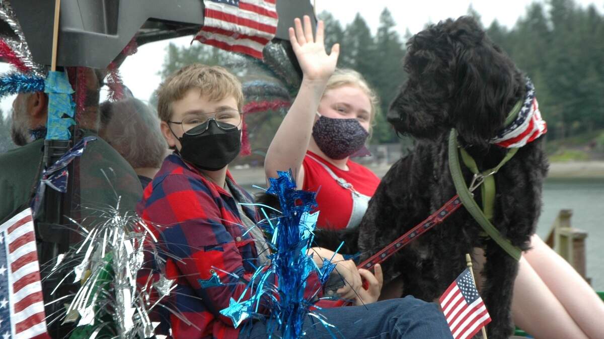 Two kids and a dog wave from the back of a decorated pickup truck during the Home 4th of July Parade.
