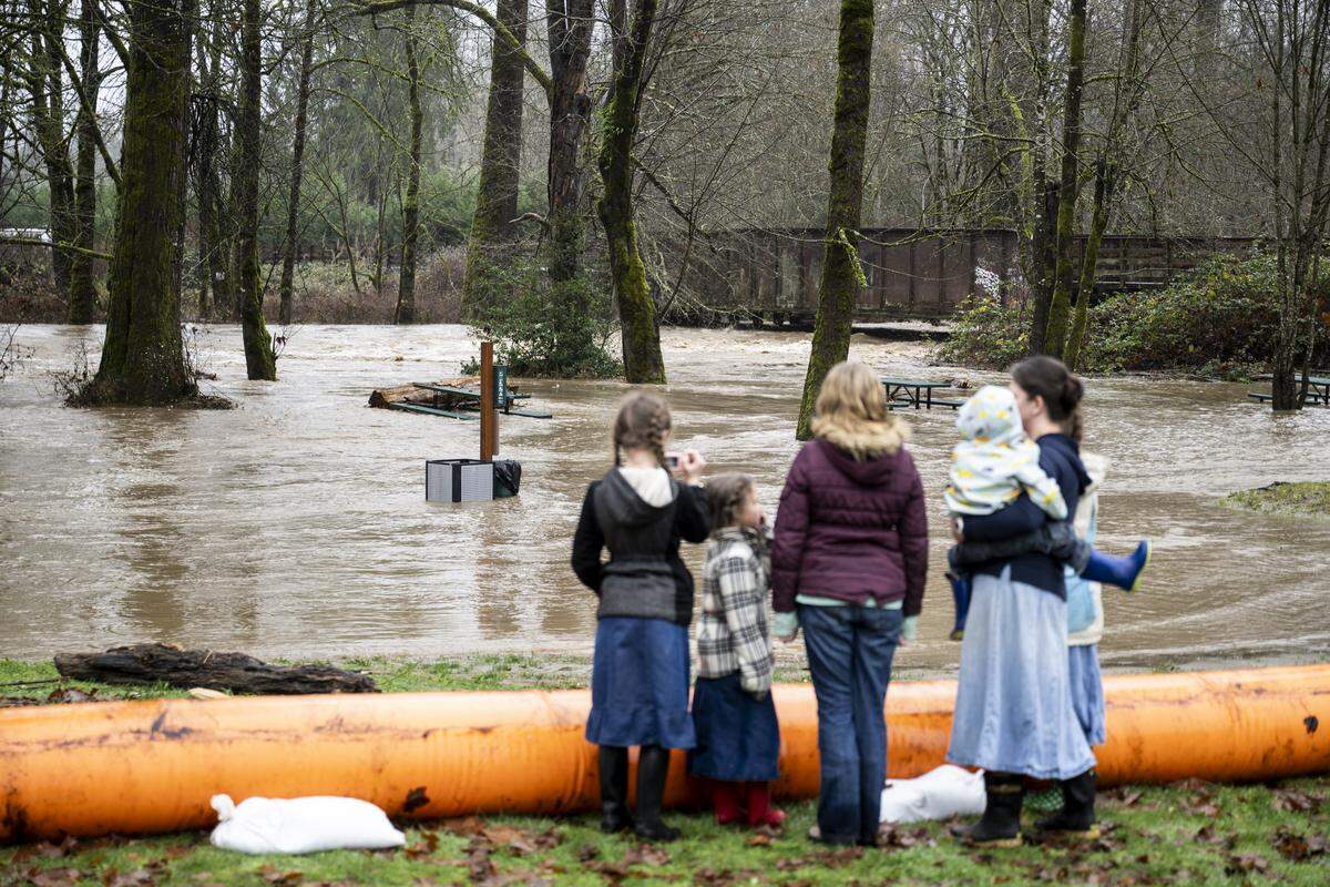 People watch as the South Prairie Creek overflows into Veteran’s Park on Thursday, Dec. 11, 2025, in South Prairie, Wash. A level 3 “GO NOW” evacuation warning is in place for homes near the South Prairie Creek.