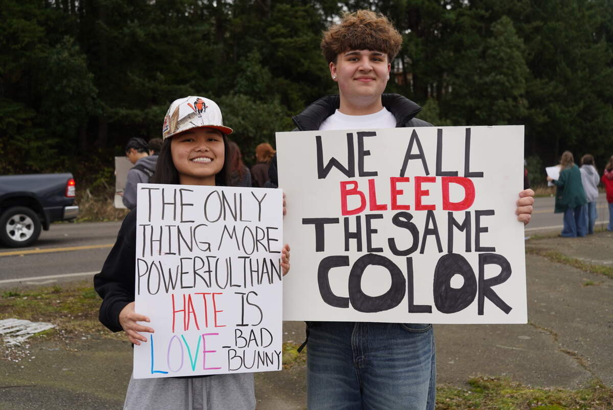 11th grader Sarang Patcharanu (left) and 10th grader Beau Newcomb (right) stand with signs at a walkout in Purdy, Wash., organized by Peninsula High School students to protest recent acts by federal immigration enforcement, Friday, Feb. 13, 2026.