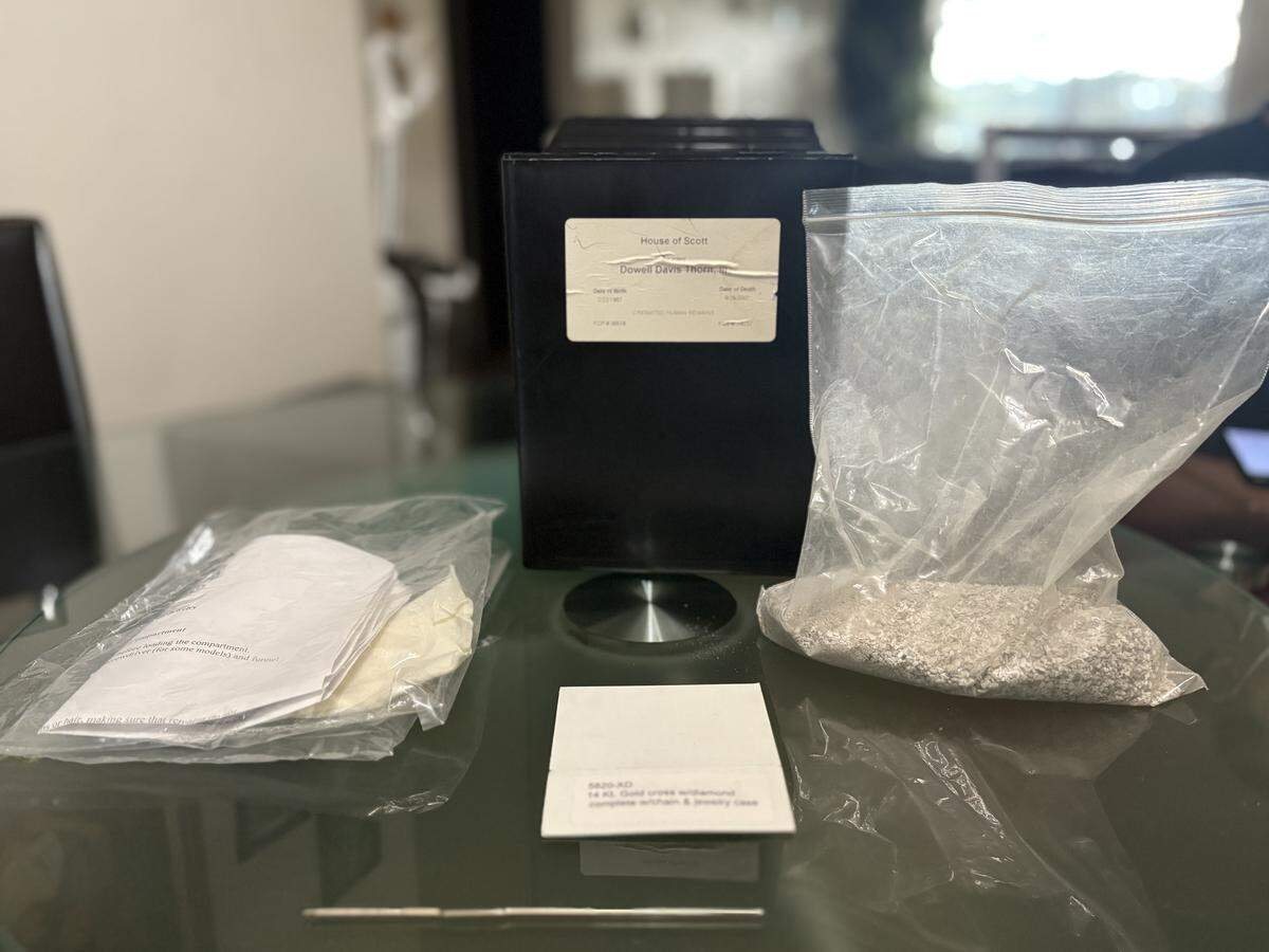 The box of Dowell “Randy” Davis Thorn III’s leftover cremated remains sits on Tiffani Robinson’s kitchen table, along with its other alleged contents. Besides a bag of his leftover ashes, the box also contained a small metal crochet hook, printed instructions for adding remains to memorial jewelry and a label for a 14-karat gold cross necklace.
