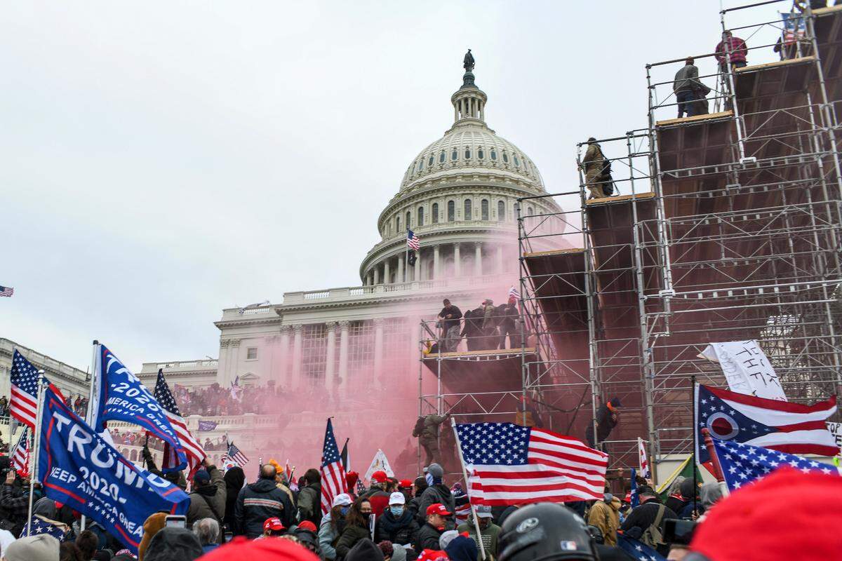 Supporters of President Donald Trump swarm scaffolding prepared for the inauguration and are met by tear gas deployed by the authorities at Capitol Building in Washington, Jan. 6, 2020.