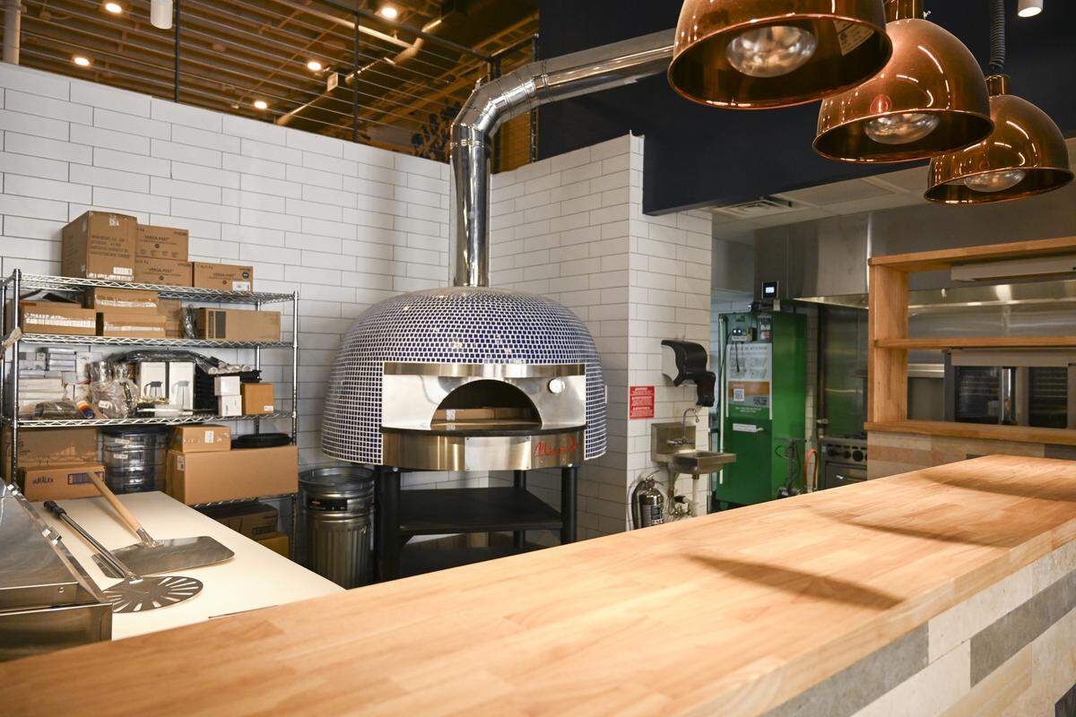 The wood-fired pizza oven anchors the open kitchen, visible right as you walk into the new Wooden City. Finishing touches were underway on April 10.