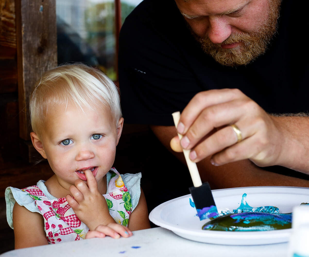 Ingrid Holm, 2, looks at the camera while Riley Holm paints a fish for Craft Saturday at the Job Carr Cabin Museum Aug. 10, 2019.