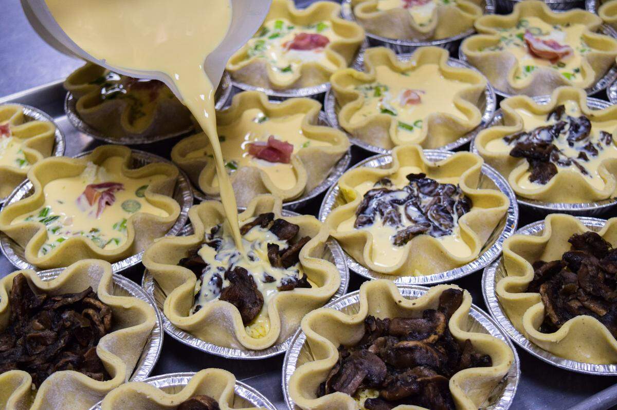 With several savory options daily, the quiche at Wren’s Nest Baking Co. is a popular choice. Camille Guerin pours in egg to shells filled with asparagus and prosciutto, mushroom and gruyere.