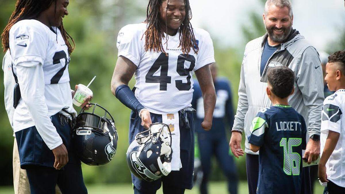 Cornerback Shaquill Griffin (26), twin brother and Seahawks teammate Shaquem Griffin (49) and Seahawks Vice President for Communications Dave Pearson talk with a young fan following Friday’s practice at training camp in Renton. The twins played together on the starting defense for the first time during the seventh practice of camp.
