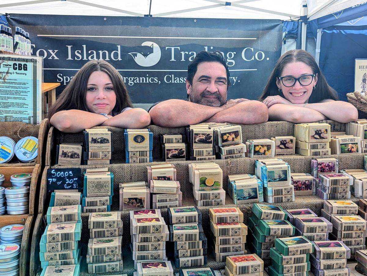 Fox Island Trading Co. co-owner Andre Hensen (middle) sells organic, all-natural bath and body products with help from Maile Olsen (right) and Sophie Olsen (left) at the Gig Harbor Waterfront Farmers Market in 2024.