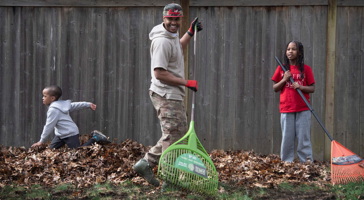 Francois Kinney rakes leaves with his children, Lauren (right) and Jalen, aka “Sonic” outside their home in Tumwater, Washington, on Tuesday, April 5, 2022.
