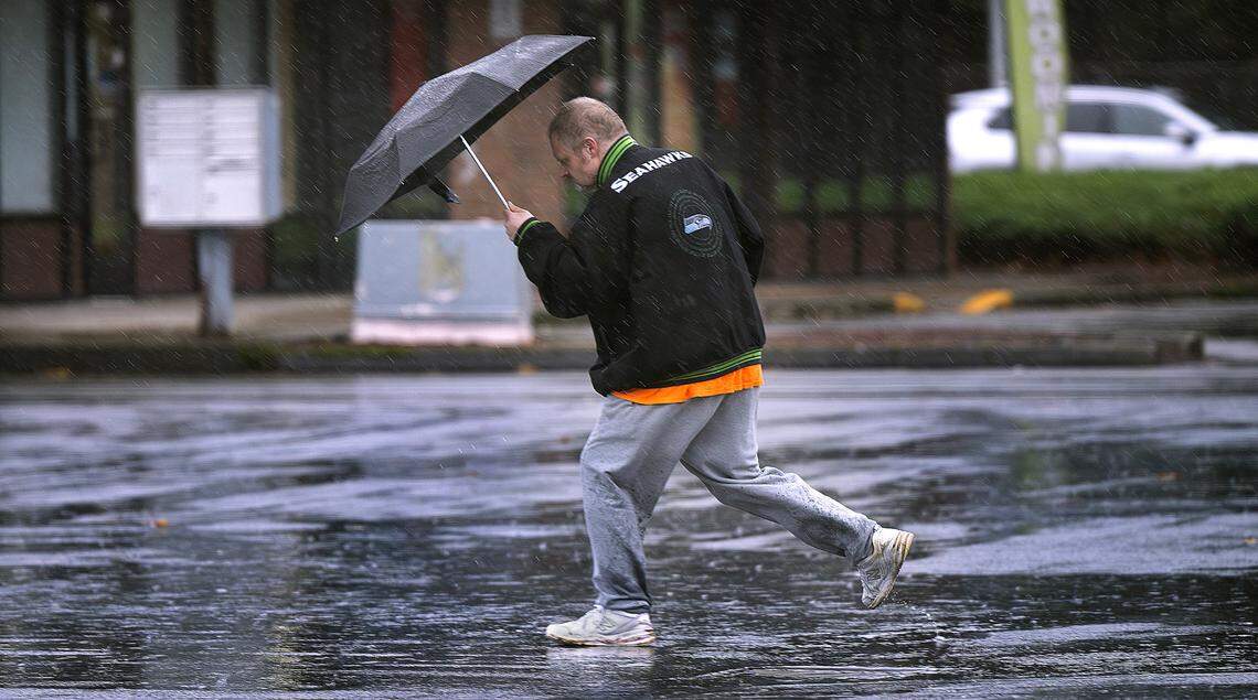 A walker dodges puddles while trying to shelter from the wind and rain in Spanaway, Washington, on Wednesday, Dec. 25, 2024.