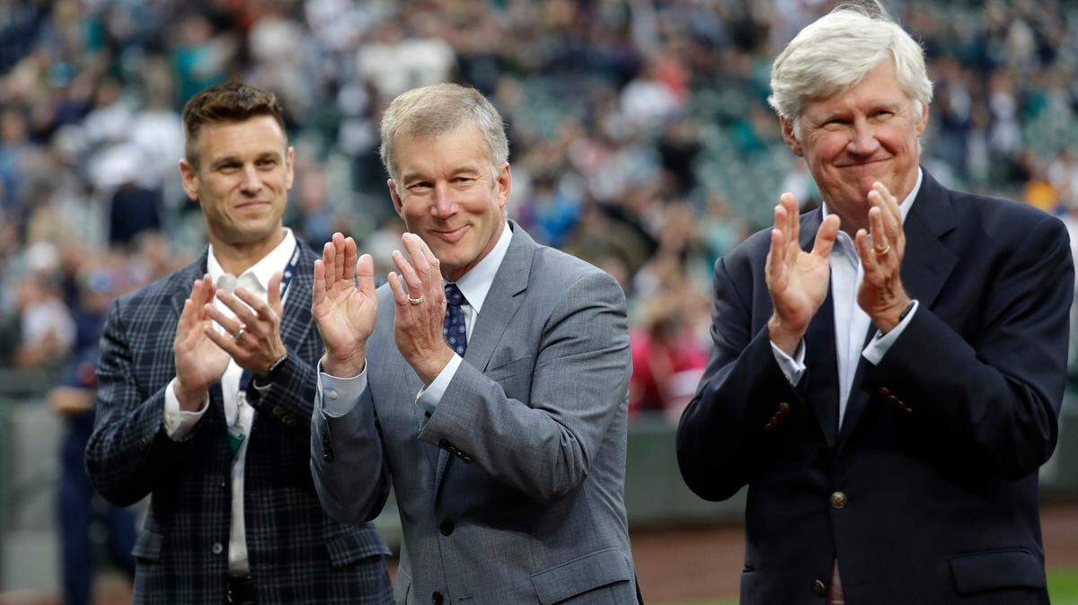 FILE - In this May 18, 2018, file photo, Seattle Mariners general manager Jerry Dipoto, left, president Kevin Mather, center, and majority owner John Stanton applaud during a presentation before a baseball game against the Detroit Tigers in Seattle. In a statement Wednesday, July 25, 2018, the Mariners say they have “made amends” with former female employees who made allegations of harassment against Mather. (AP Photo/Elaine Thompson, File)