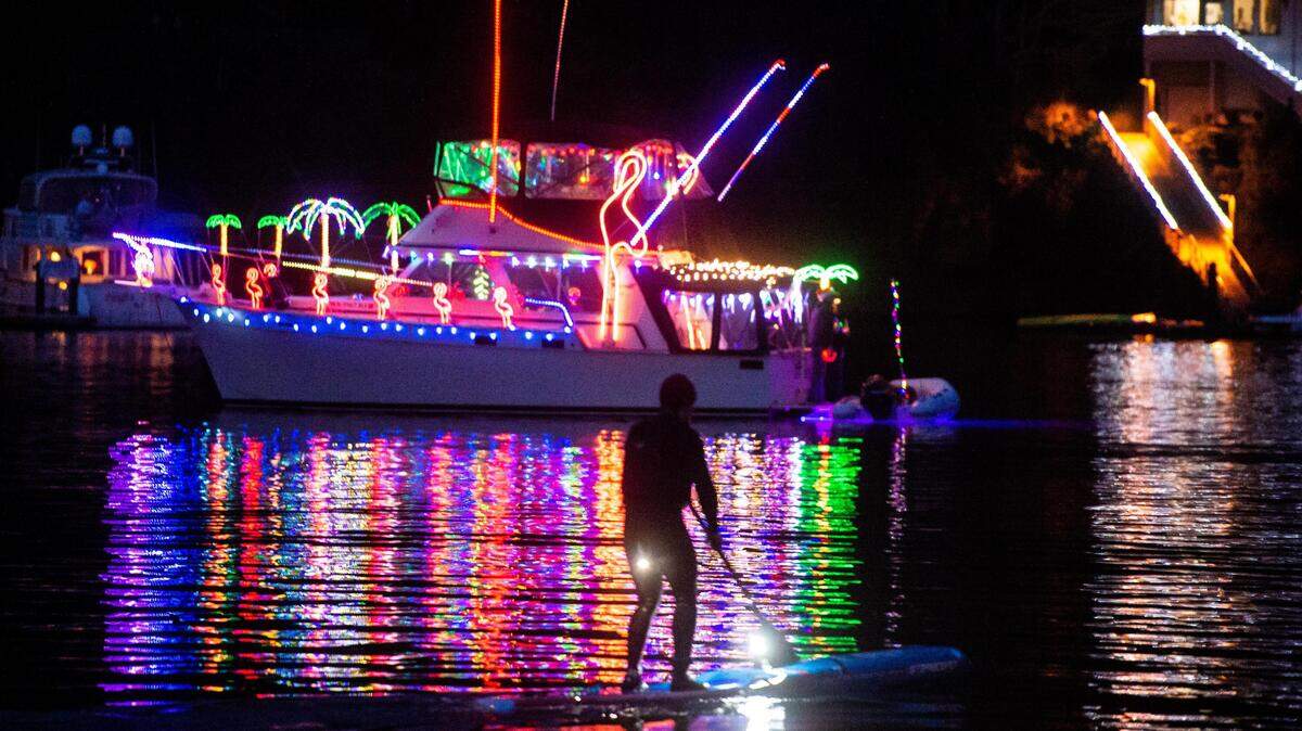 A paddle-boarder passes by as decorated boats pass by the dock near Skansie Brothers Park during the annual lighted boat parade in Gig Harbor on Saturday. For more holiday events, see the Peninsula Calendar, inside.