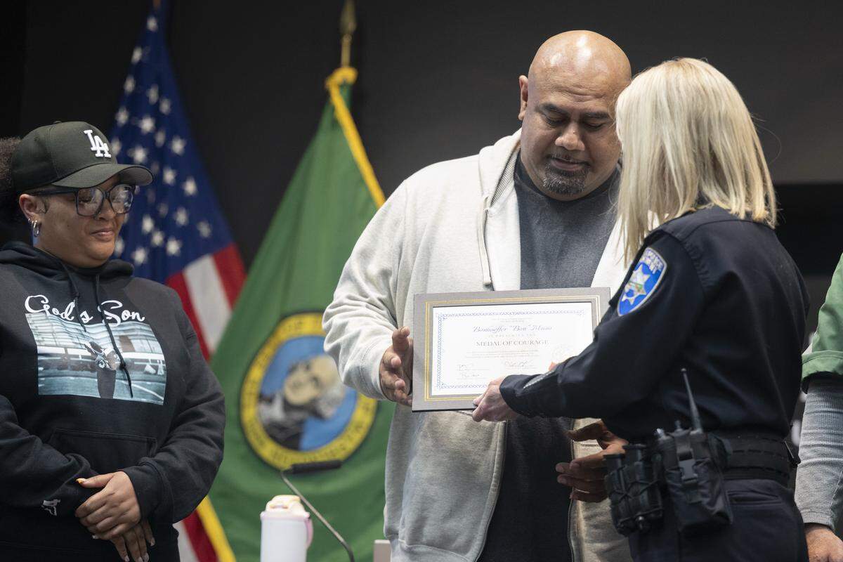 Foss High School campus security guards Sharrese LuRee Johnson, left, and Bonhoeffer (Bon) Muao receive a certificate from Police Chief Patti Jackson, right, on Thursday, May 14, 2026, for intervening during an aggravated assault at Foss in April. Johnson and Muao received the Medal of Courage, alongside other staff members.