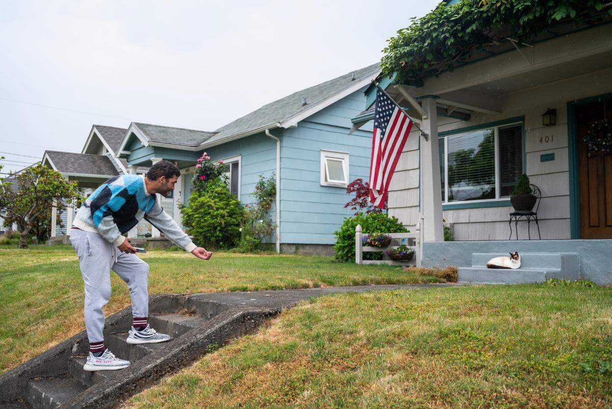 Chris Watson, Tiktoker and founder of the Catluminati, reaches his hand out as he trys to coax “Man Cat” the cat off of his porch steps while he naps in Tacoma, Wash. on July 5, 2022.